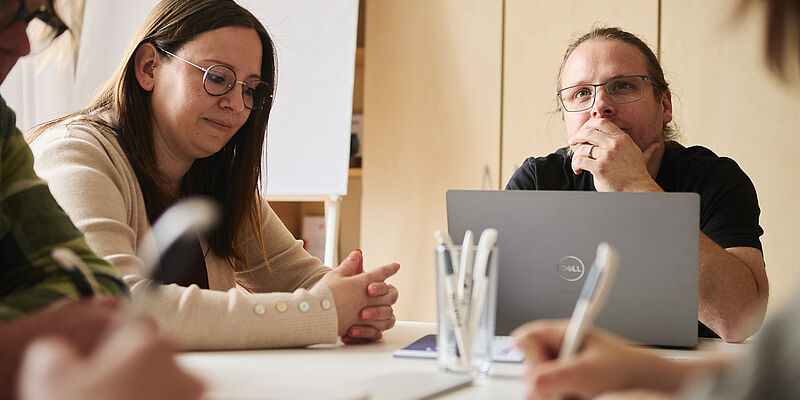 Mehrere Mitarbeitende von Fortis sitzen an einem Tisch und unterhalten sich. Ein aufgeklappter Laptop, Stifte und Papier sind sichtbar.